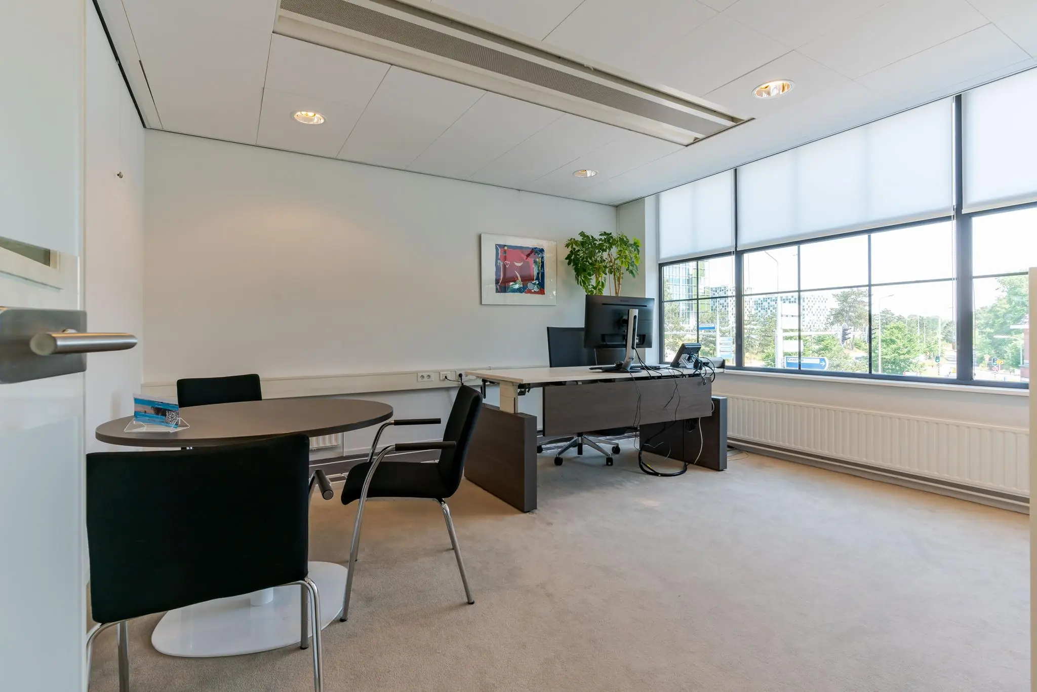 Modern kantoor aan de Van Alkemadelaan met bureau, vergadertafel, grote ramen en veel daglicht.